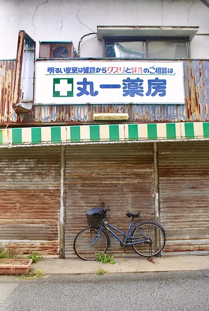 「丸一薬房」の看板と、さびたシャッターに立てかけた自転車