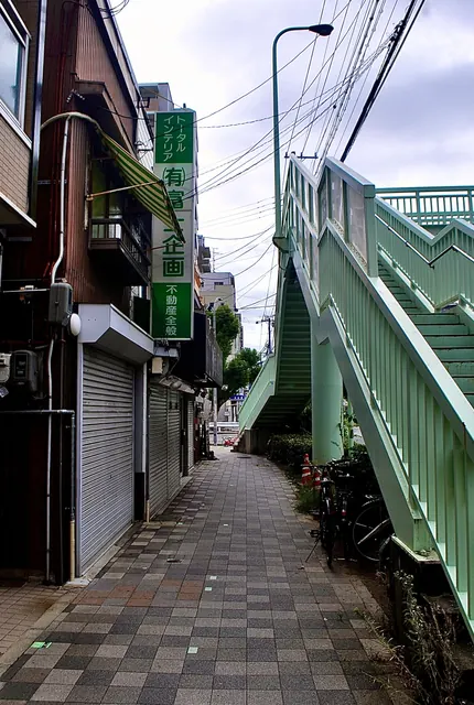 緑の歩道橋の脇を、奥へ続くタイルの歩道