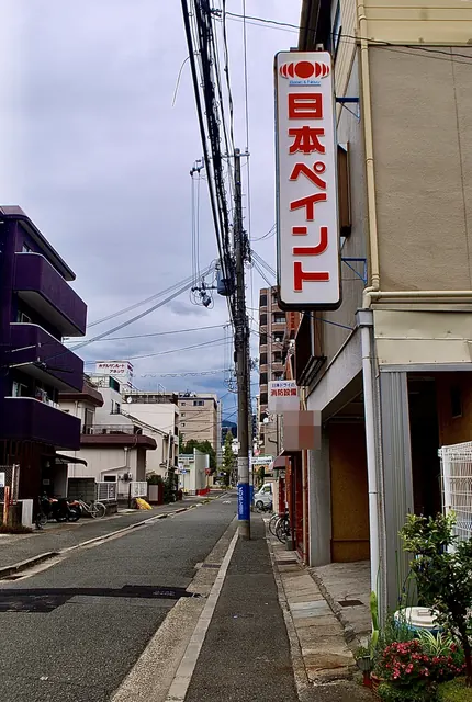 赤い「日本ペイント」の縦看板と、奥へ続く住宅街の道