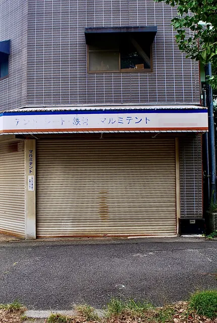 「マルミテント」の看板と、古いシャッターが残る店