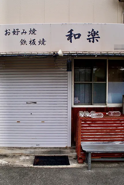 「お好み焼 鉄板焼 和楽」の看板と、赤いベンチの店先