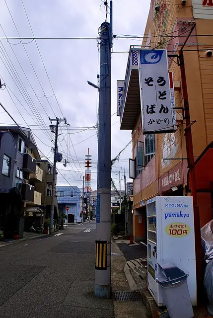 「うどん そば」の看板と自動販売機が並ぶ、細い道