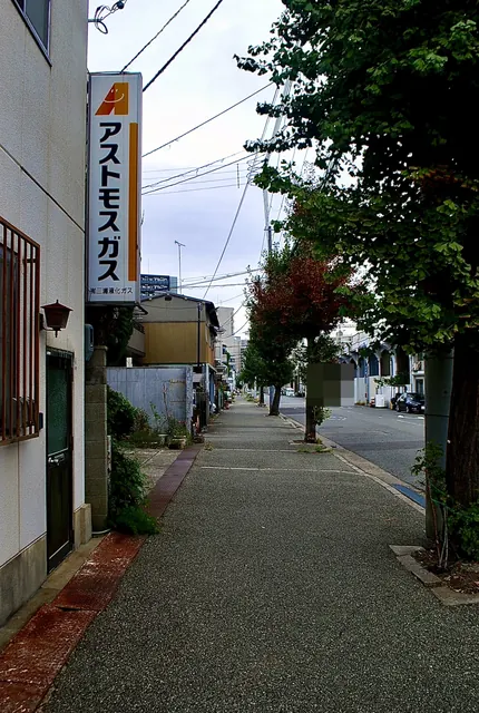 黄色い「アストモスガス」の看板と、並木の続く歩道