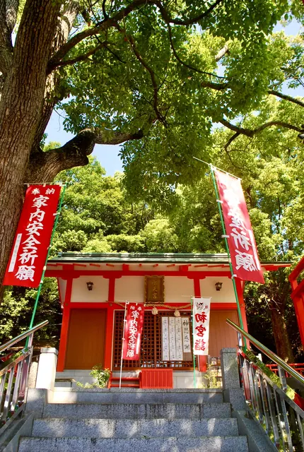 大きな木々の下にたたずむ、朱色のお社と赤い幟
