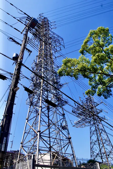 濃い青空の下、電線を張りめぐらせた鉄塔を見上げる風景