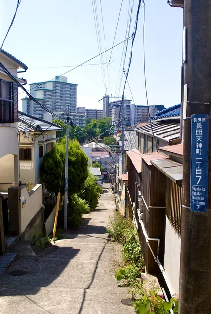 町名表示のある電柱の脇から、団地の見える坂の路地