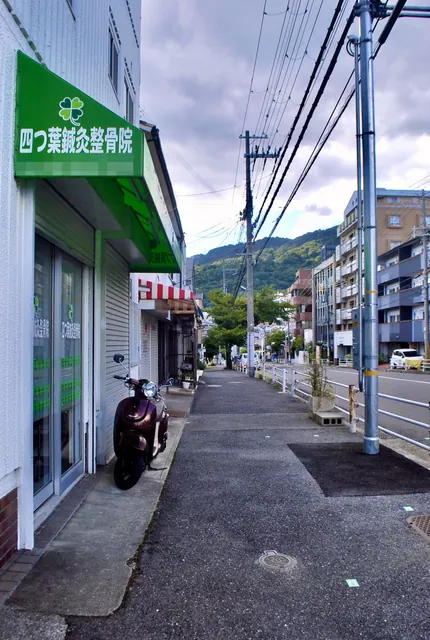 緑の日よけの店の前を、山の見える奥へまっすぐ続く歩道