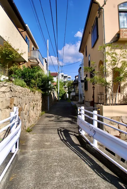 石垣と白いガードレールに挟まれ、青空の下を奥へ続く路地