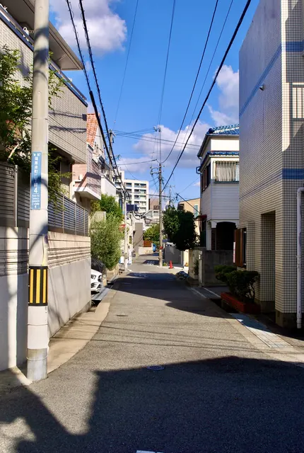 町名表示のある電柱の脇から、青空の下をまっすぐ続く住宅街の通り