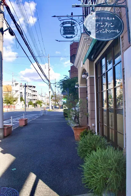 装飾のある吊り看板の店先と、植木鉢の並ぶ広い歩道