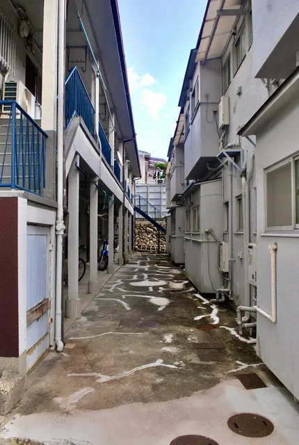 二棟のアパートに挟まれ、奥の石垣と階段へ続く細い路地