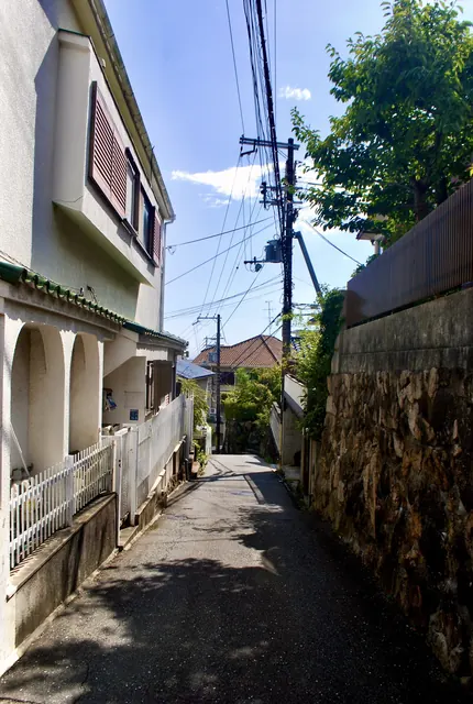 アーチのある家と石垣のあいだを、木陰の奥へ続く路地