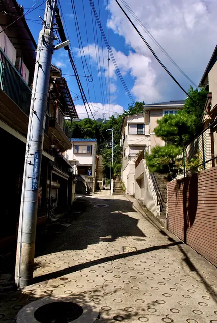 町名表示のある電柱の脇から、丸い滑り止めの坂が石段へ続く風景