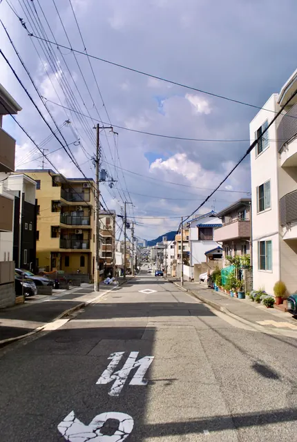 電線の張られた空の下、奥に山の見える住宅街の通り