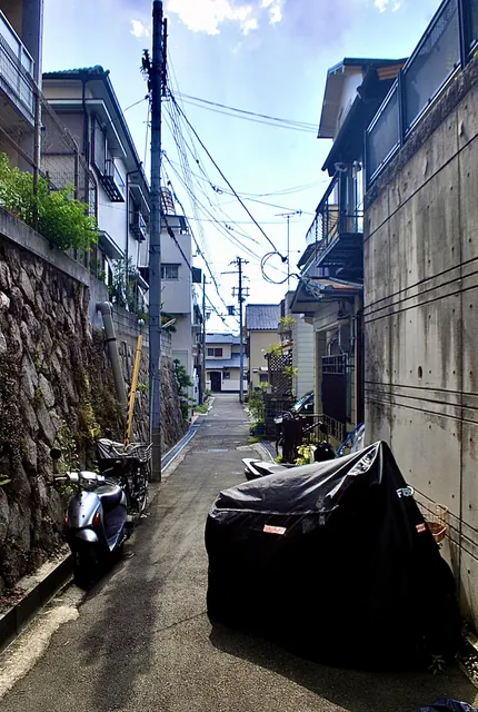 石垣の脇にスクーターが並び、電線の下に続く細い路地