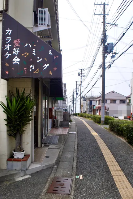 音符の描かれた「カラオケ愛好会」の看板と、点字ブロックの歩道