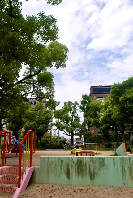 大きな木々に囲まれ、遊具の並ぶ公園