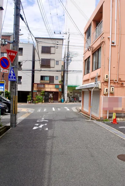 シャッターの店とピンクの建物が並ぶ、静かな交差点