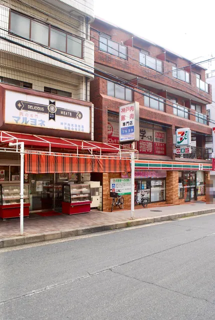 大きな看板の精肉店と、赤い縞の日よけが並ぶ商店街の店先