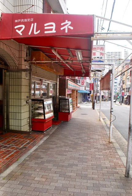 赤い日よけの精肉店の前から、奥へ続く商店街の歩道