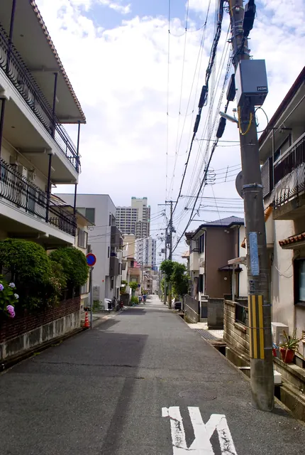 電柱と家々が並び、奥のマンションへまっすぐ続く通り