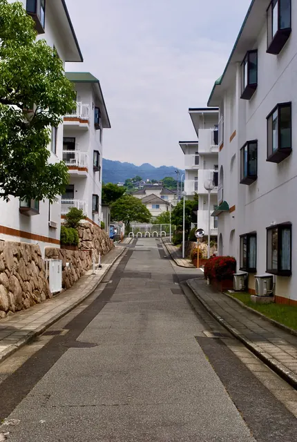 白い建物に挟まれた坂道の先に、山並みが見える風景