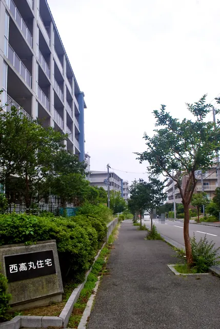 「西高丸住宅」の銘板と、団地に沿って続く並木の歩道