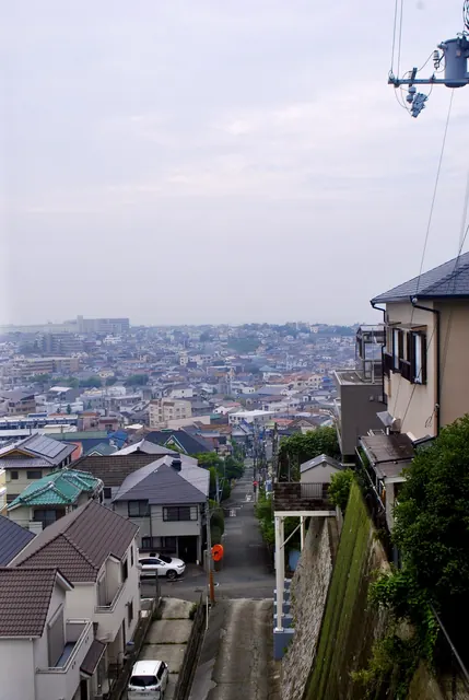 急な坂の上から、段々に重なる屋根と遠くの街並みを見る風景