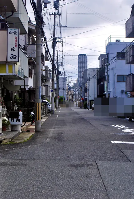 お店の看板の先に、電柱と家々がまっすぐ続く住宅街の道