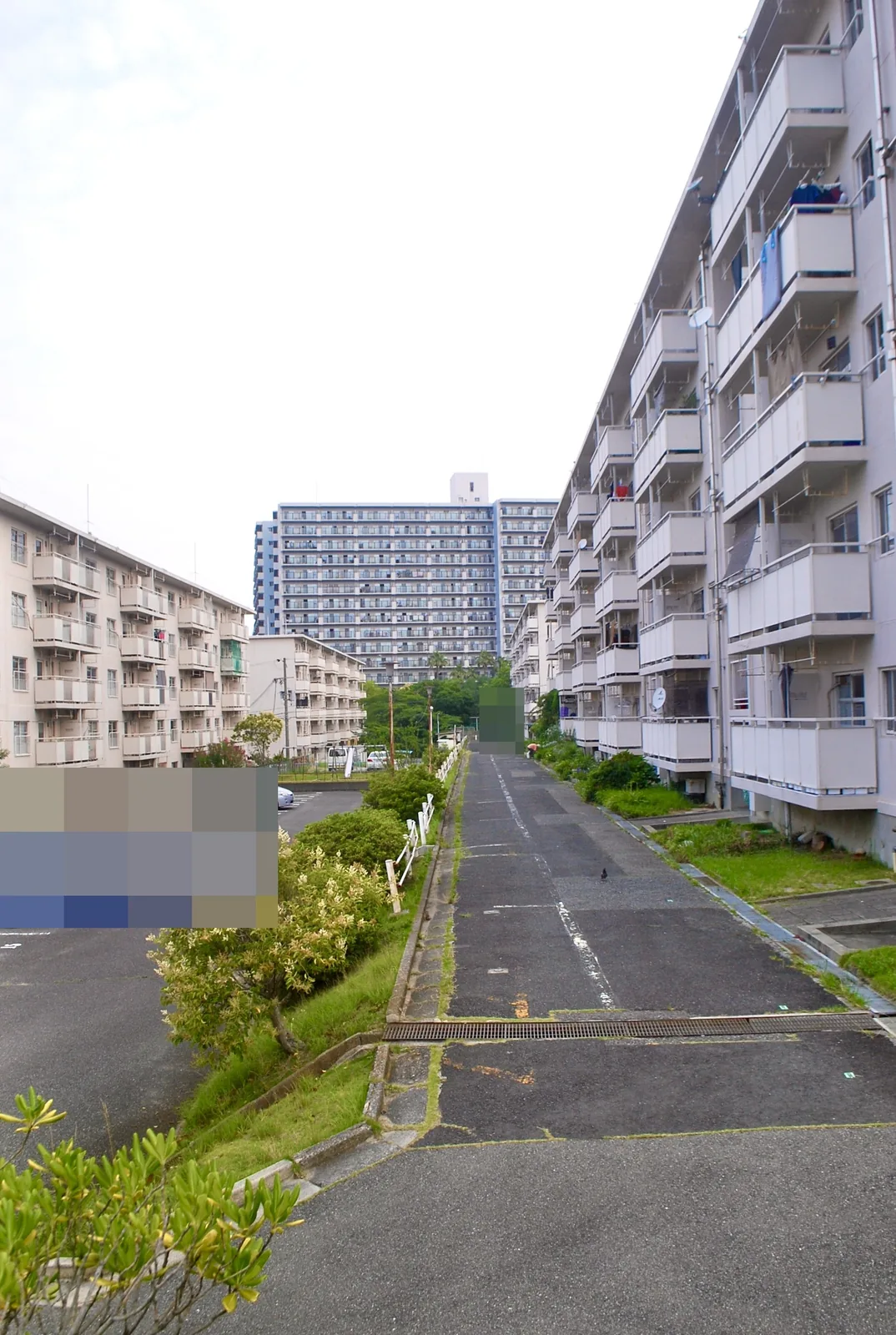 団地と駐車場のあいだを、奥の高層住宅へ上る細い坂道