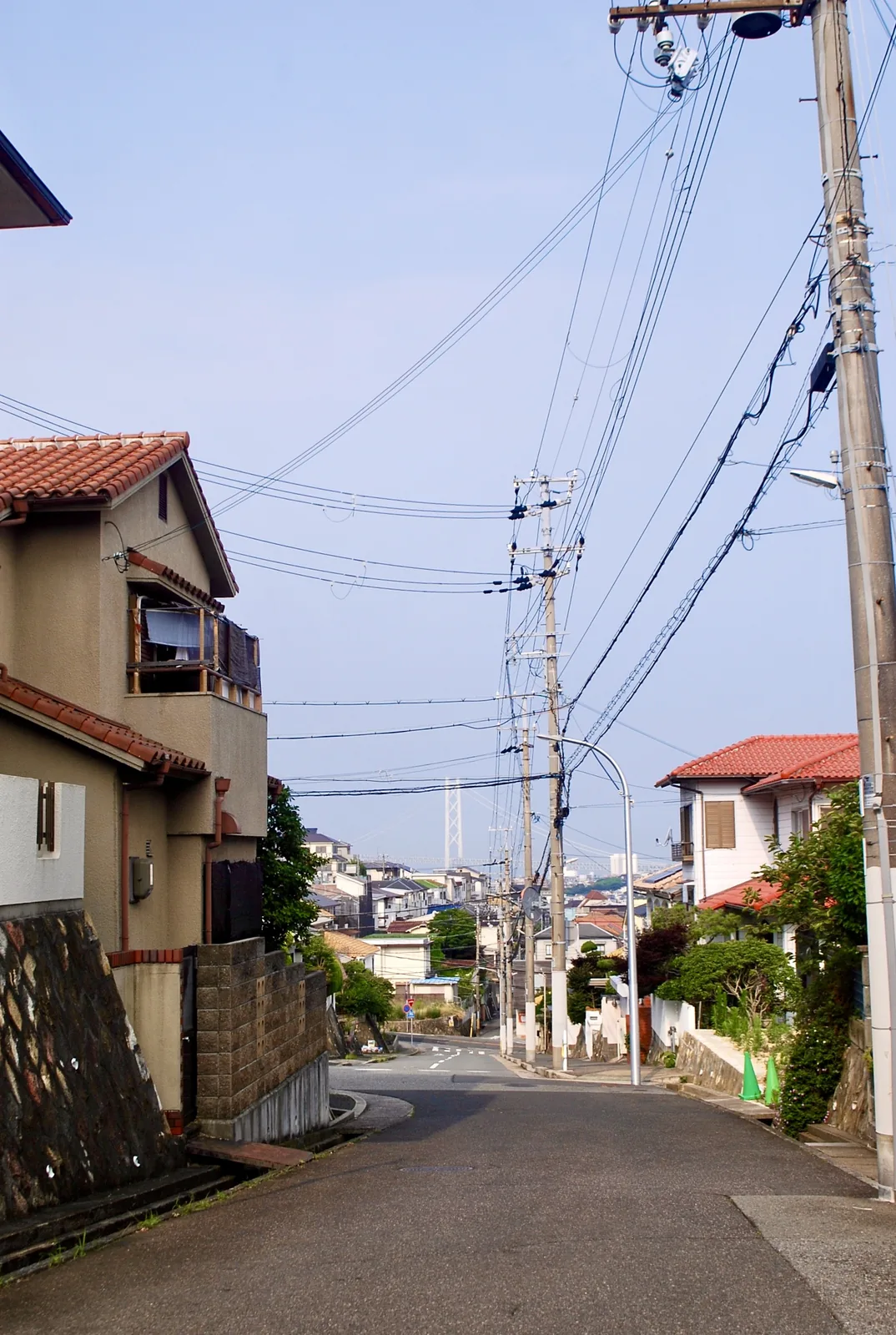カーブする坂道と家々の向こうに、明石海峡大橋の主塔が見える風景