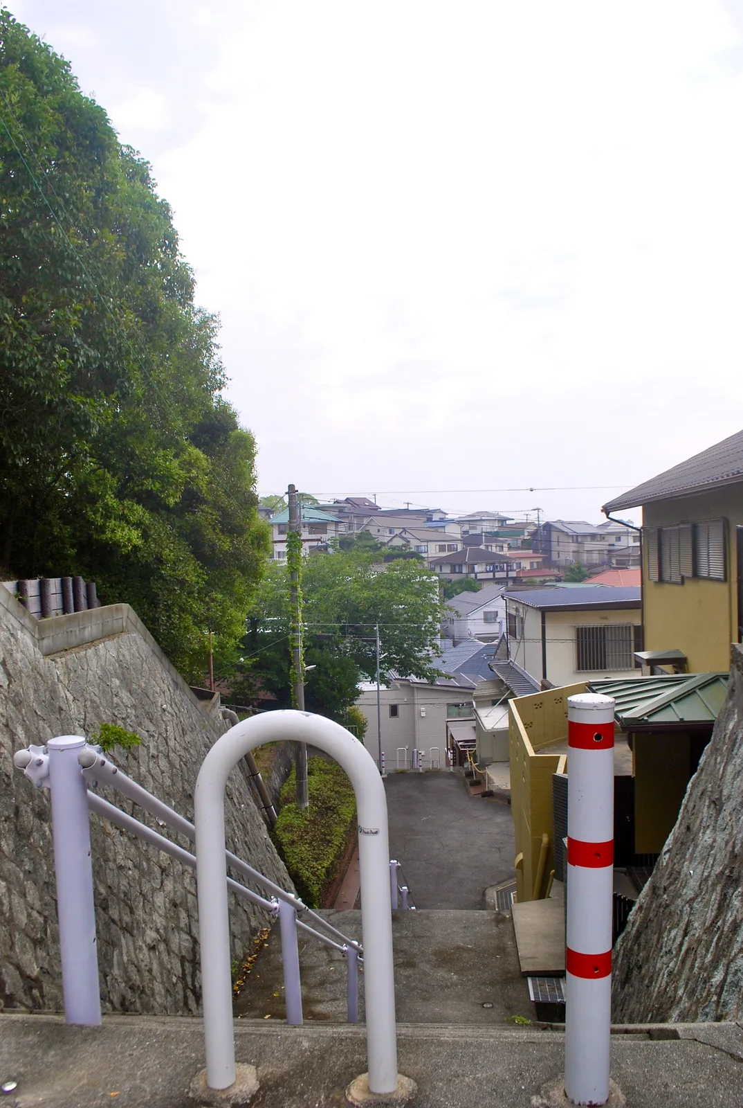 石垣のあいだを下る階段の先に、丘の家並みが広がる風景