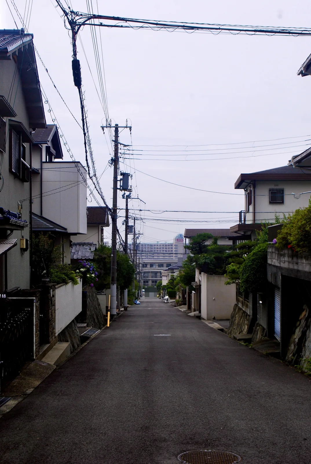 電柱と家々が並び、奥の建物までまっすぐ続く坂道