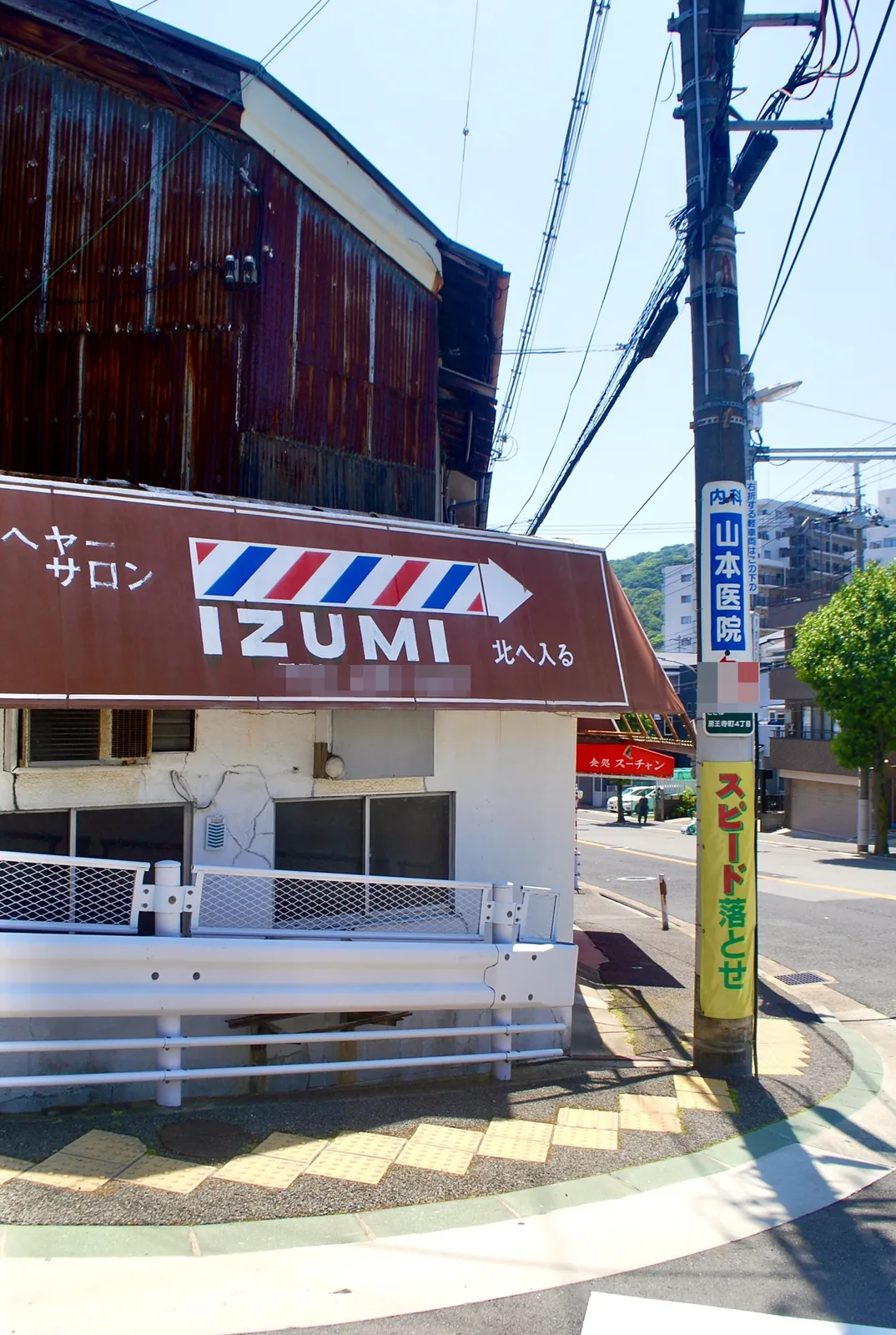 サインポール柄の大きな看板と、トタン壁の古い建物