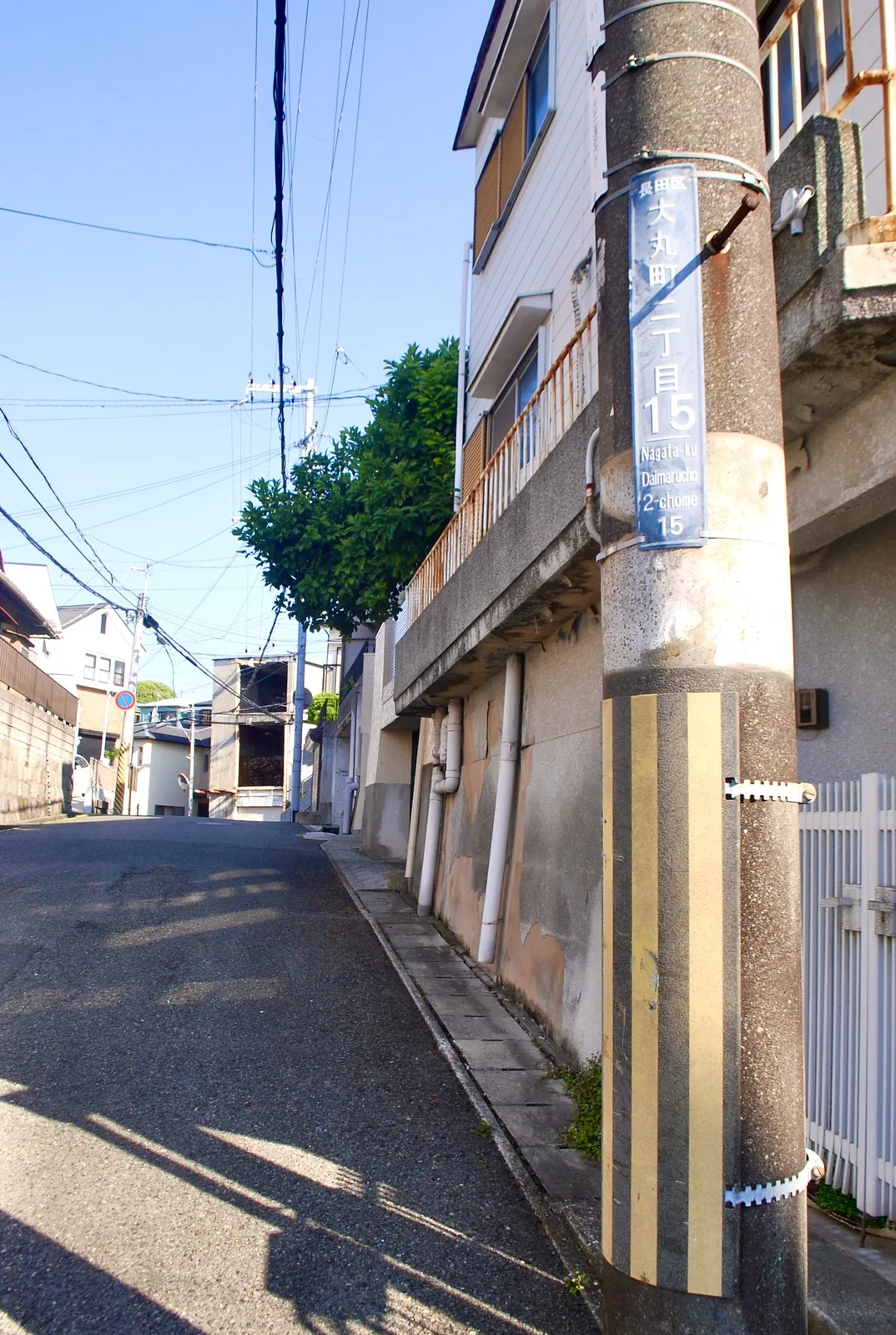 電柱と家々に挟まれ、下っていく住宅街の坂道