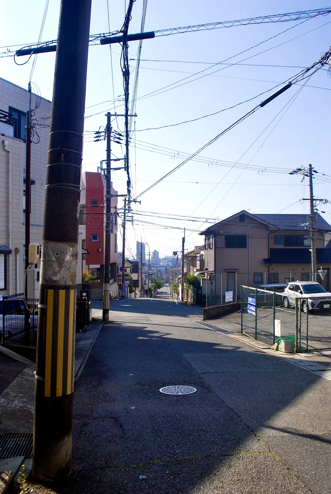 電柱と電線の並ぶ交差点の先に、遠くの街並みが見える風景