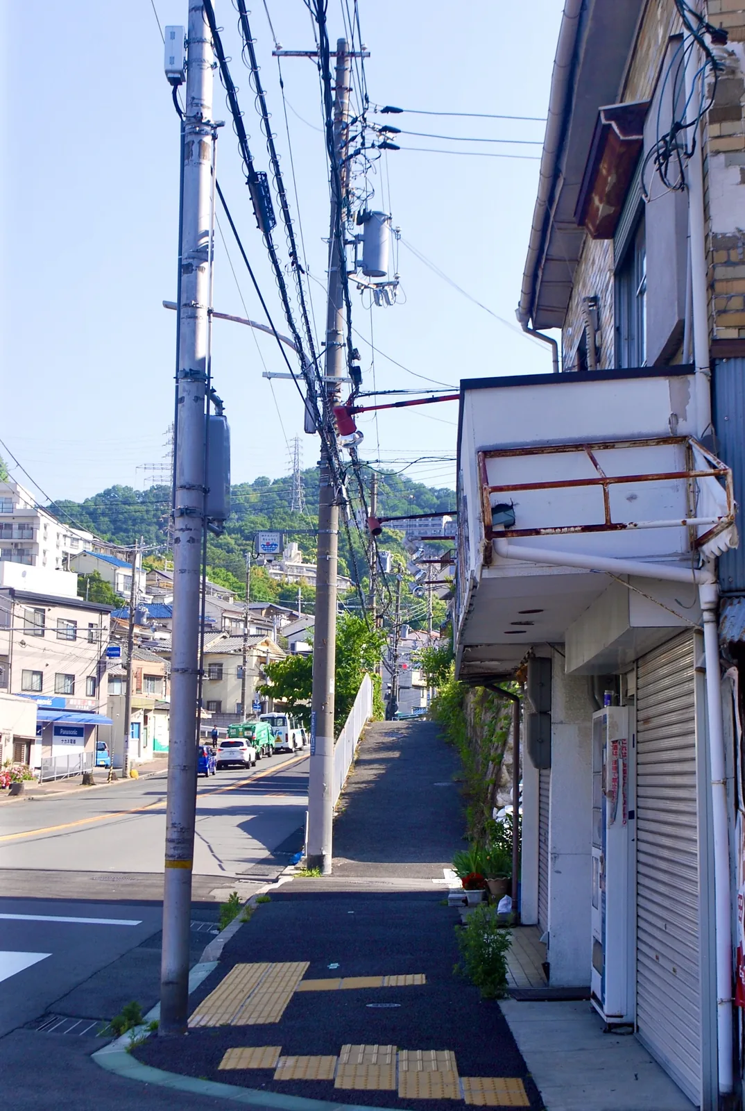 シャッターの店が並ぶ通りの先に、緑の山が見える風景
