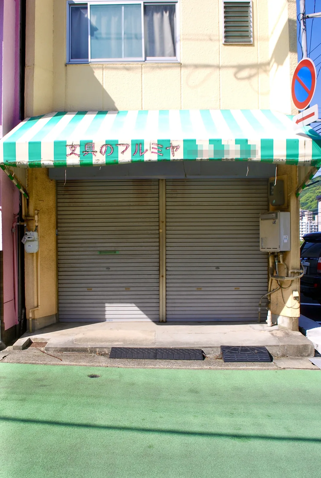 緑と白の縞の日よけの下で、シャッターの下りた文具店