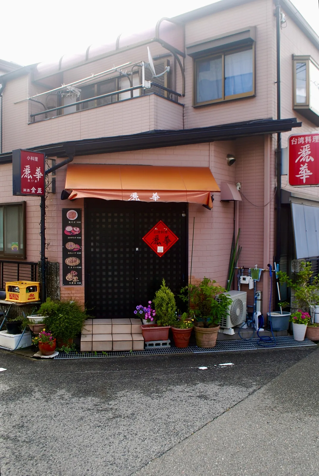 オレンジの日よけと赤い飾り、植木鉢が並ぶ台湾料理の店先