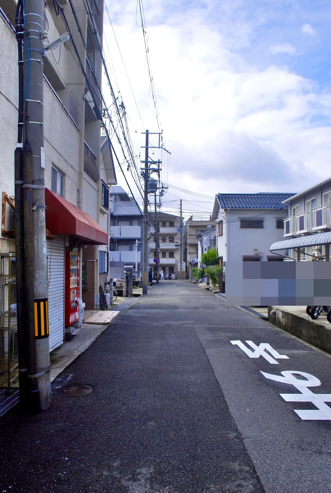 赤い日よけと自動販売機の店先から、まっすぐ続く住宅街の道