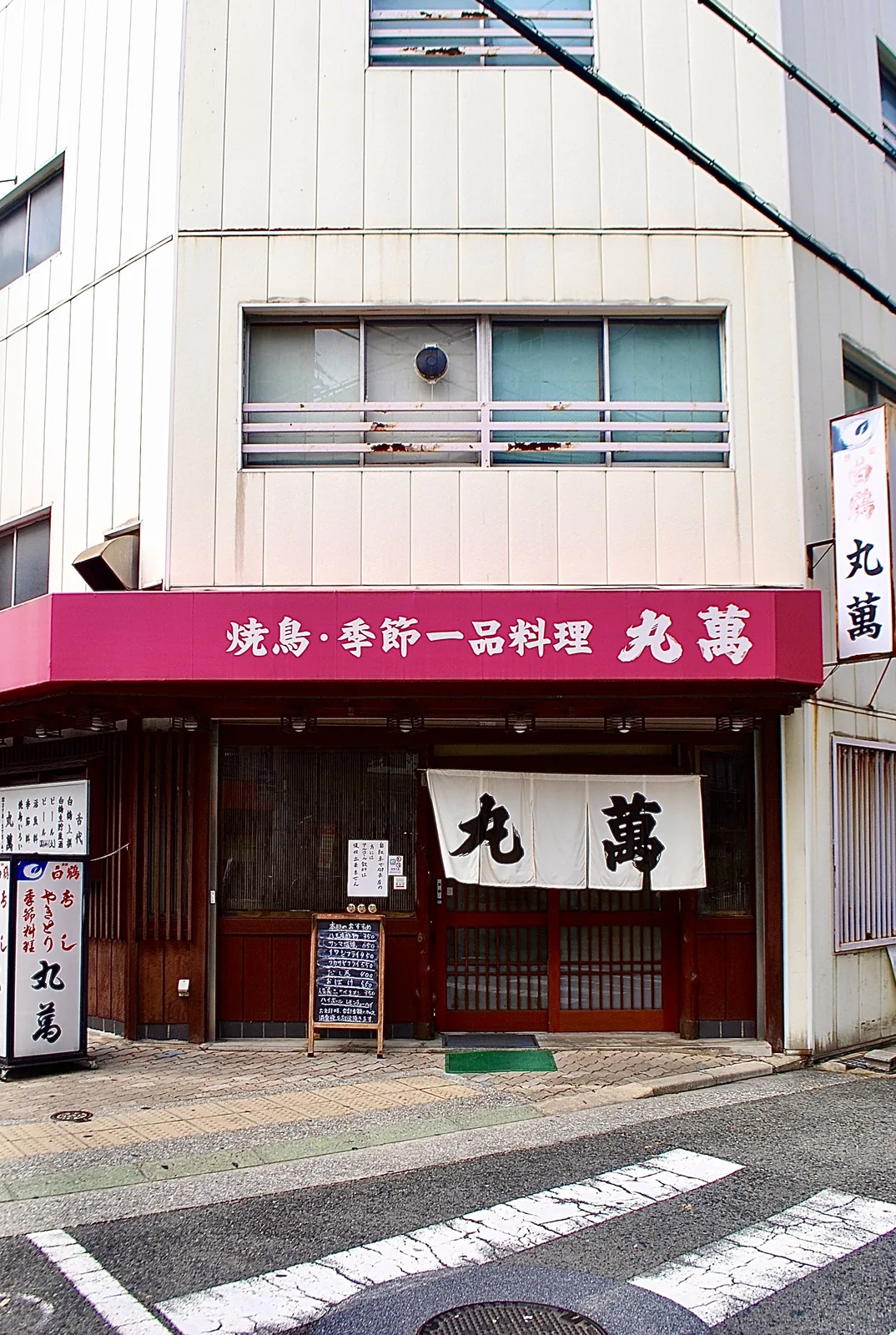 ピンクの日よけと大きなのれんの、焼き鳥・一品料理の店