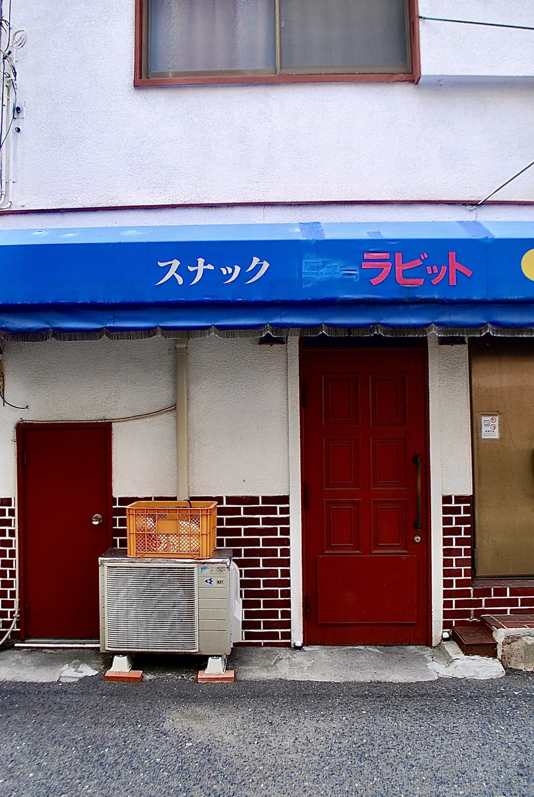 青い日よけと赤い扉、レンガ模様の壁の店