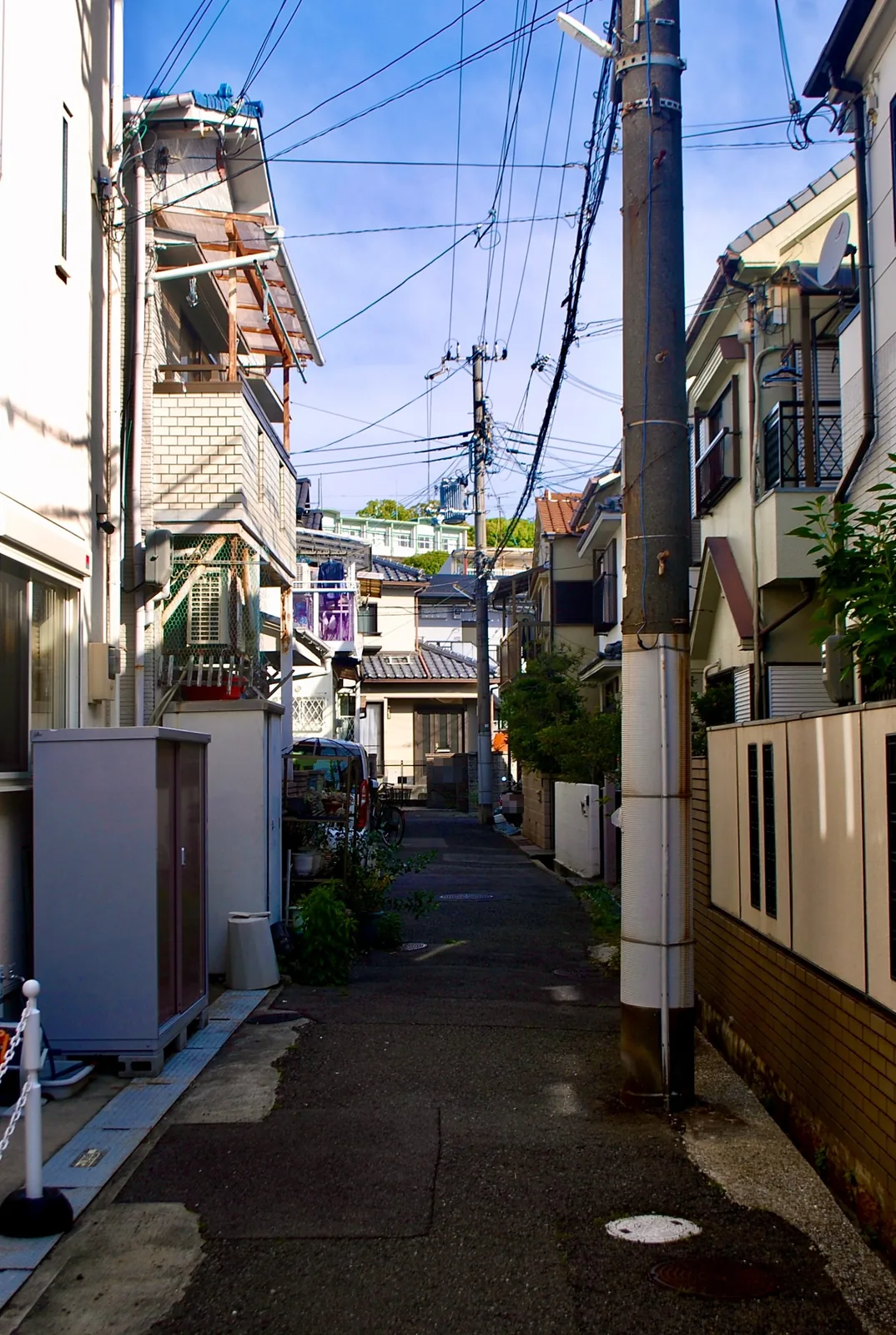 電柱が立つ細い路地。奥に瓦屋根の家が見える