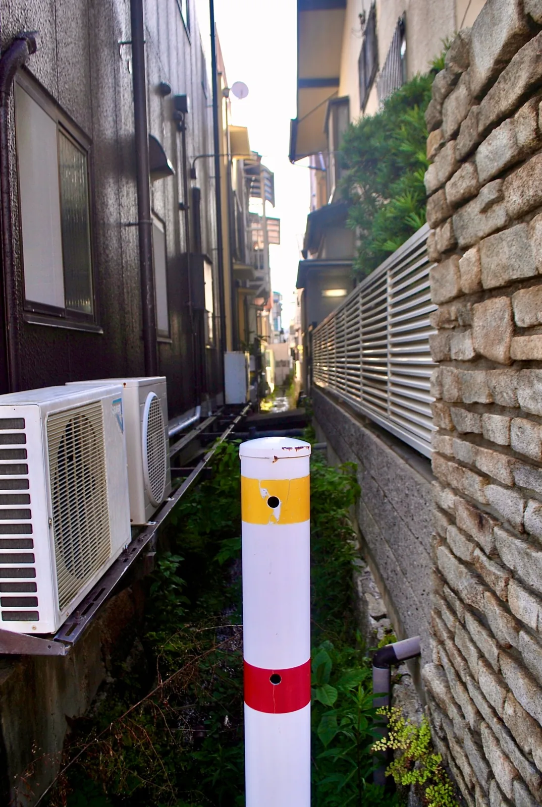 家と家のあいだの細い水路と、手前に立つ白いポール