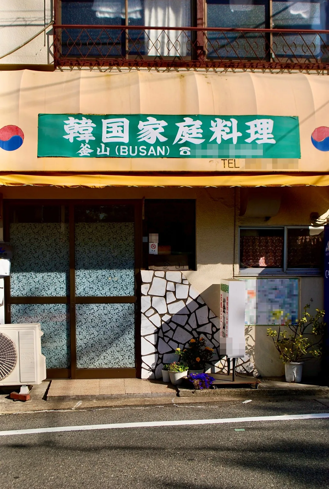 緑の看板と植木鉢が並ぶ店先