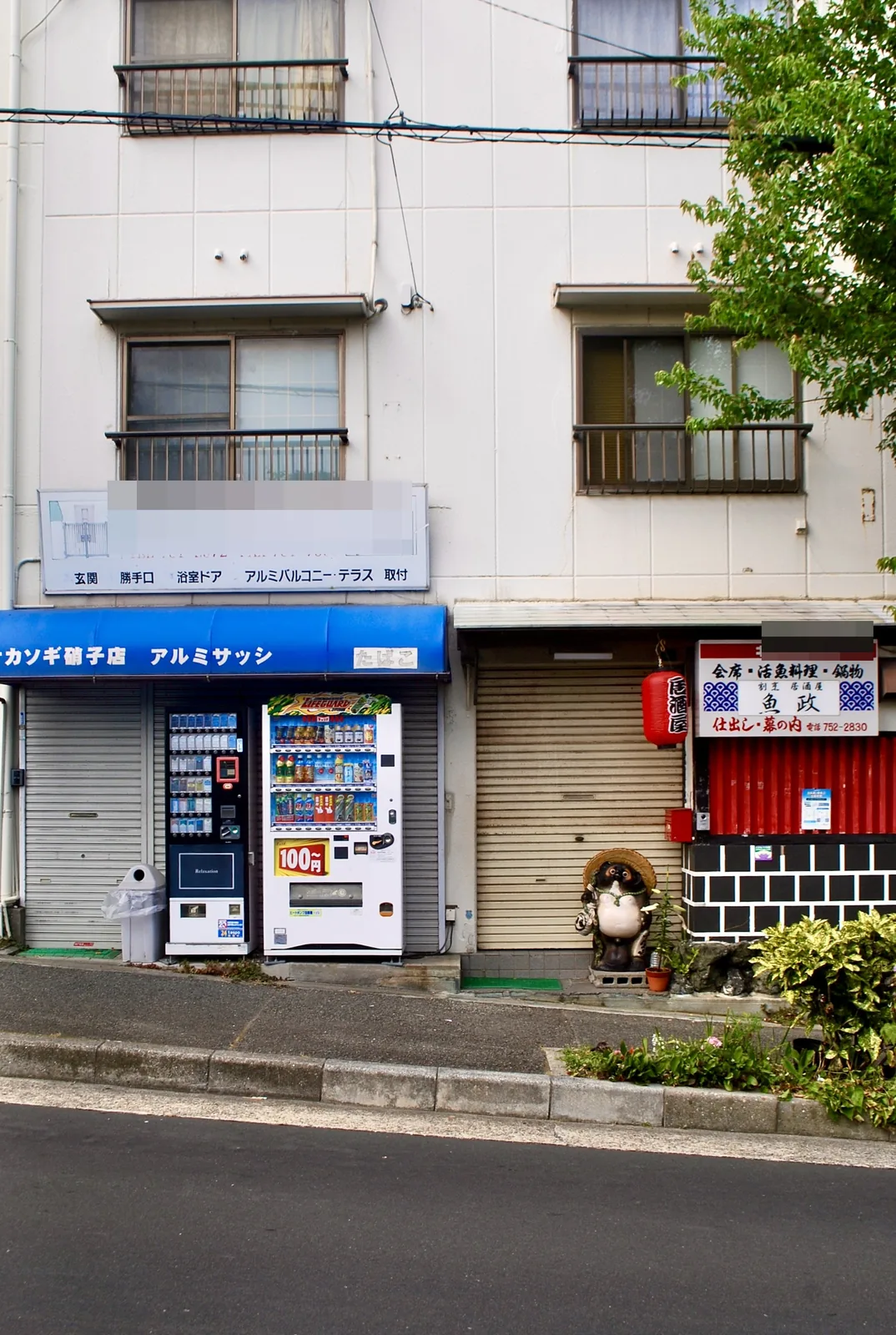 硝子店の青い日よけと、たぬきの置物と赤い提灯のある割烹居酒屋