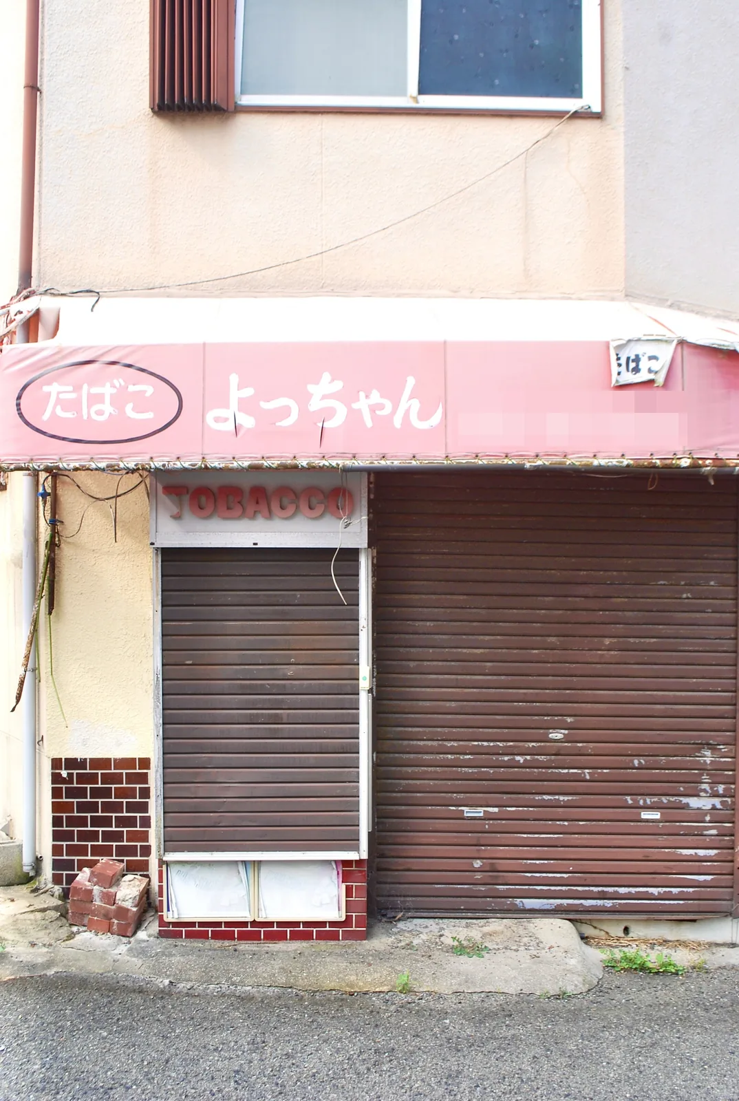 ピンクの日よけに「たばこ よっちゃん」と書かれた、シャッターの店