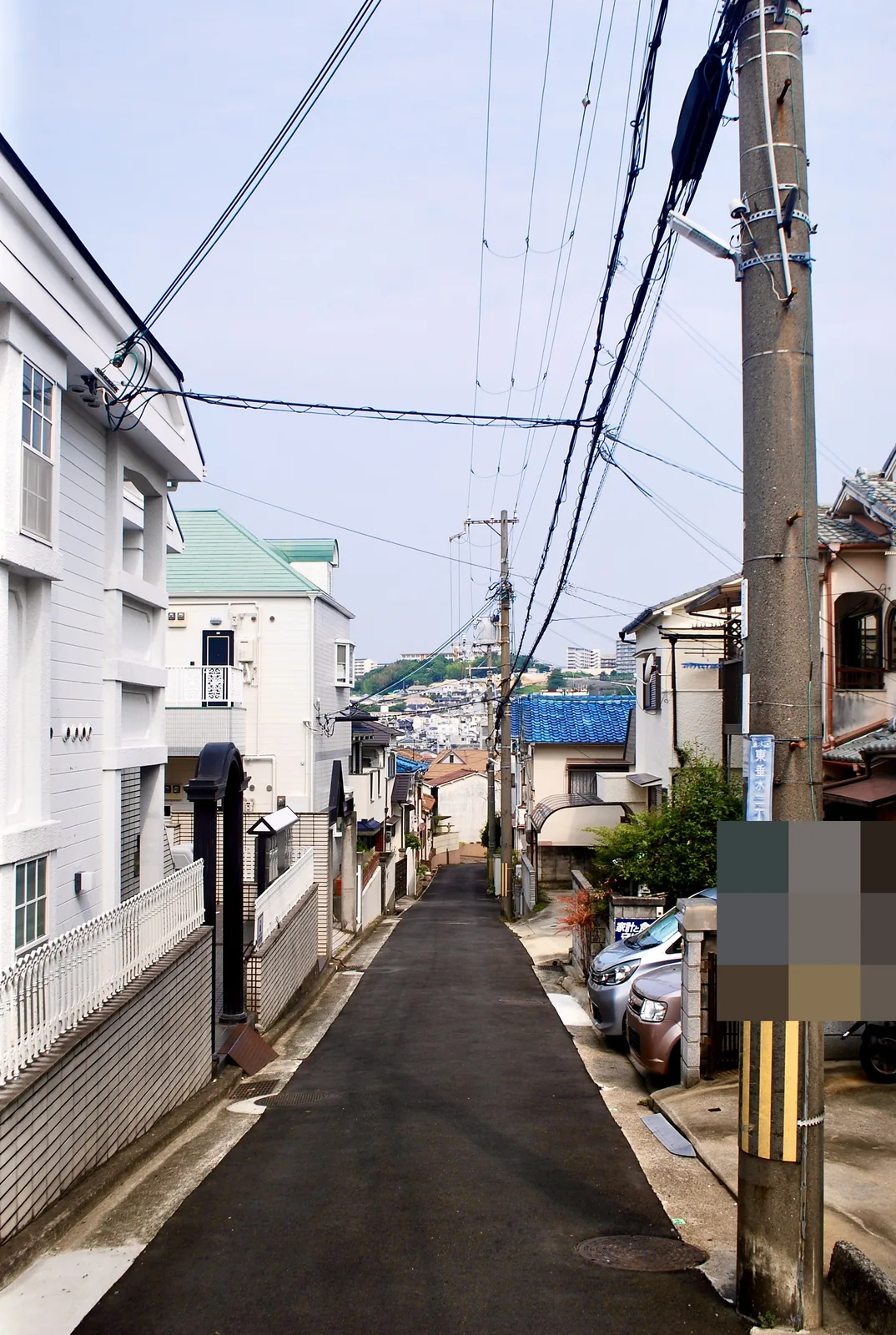 白い柵の家々のあいだから、遠くの街並みへ下る細い道