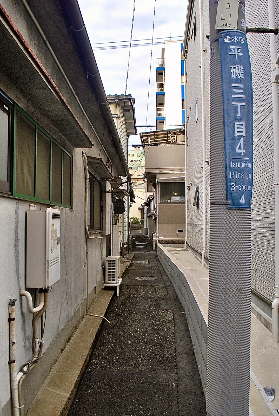 町名表示のある電柱と、家の壁に挟まれた細い路地