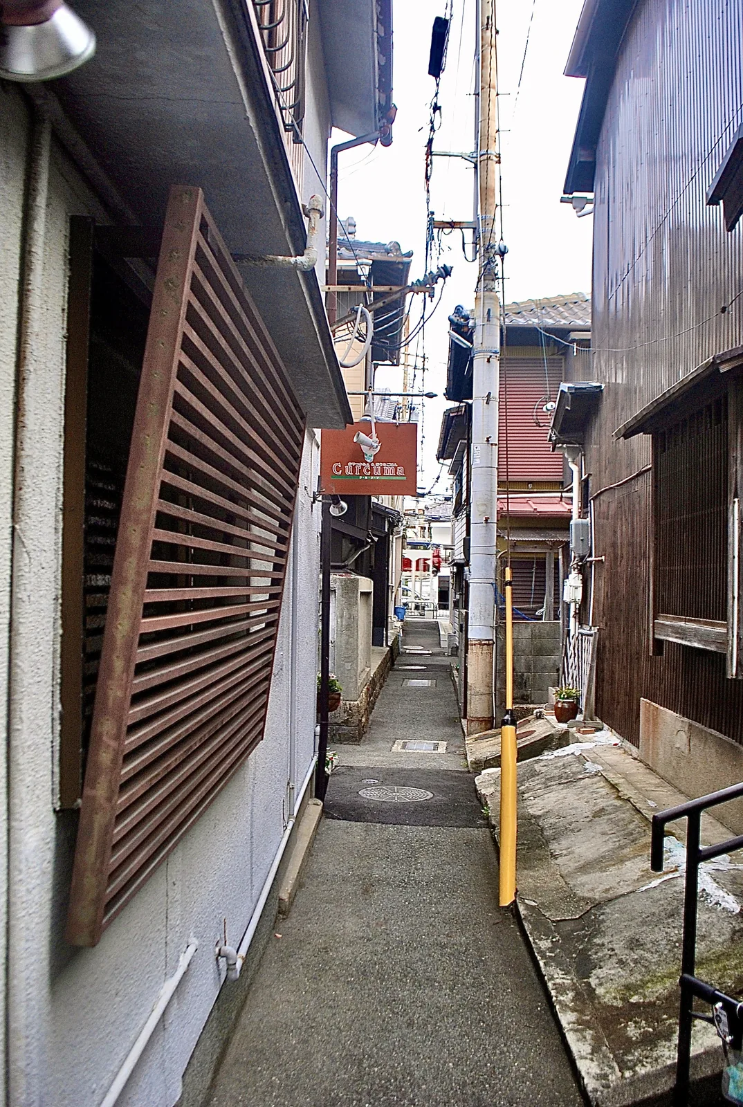 木の格子窓の家の脇に、小さな吊り看板が下がる路地